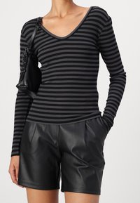 Svart och grårandig långärmad topp med V-ringning, matchad med högmidjade svarta skinnshorts. Har en strukturerad axelväska.