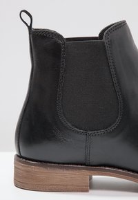 Schwarzer Stiefelette aus Leder mit elastischem Einsatz, abgerundetem Zehenbereich und gestapeltem Holzabsatz. Glatte Textur mit dezenten Nahtdetails.