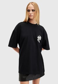 Černé oversized tričko vyrobené z bavlny, s bílým grafickým akcentem na hrudi, krátkými rukávy a uvolněným střihem.