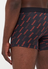 Svarta kalsonger med röd "Levi's"-logotyp. Elastiskt midjeband, mjukt tyg, åtsittande design och synliga sömmar.