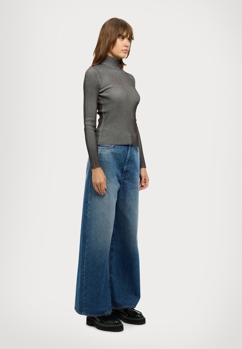 Col roulé slim, côtelé, gris métallisé associé à un jean en denim bleu délavé à jambe large. Chaussures à plateforme noires brillantes. Fond simple.