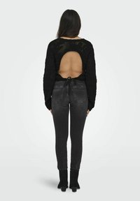 Maglione nero a maglia con schiena scoperta e dettaglio annodato, abbinato a jeans skinny scuri e stivaletti neri. Tessuto liscio su tutta la superficie.