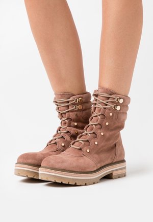Semišové kotníkové boty v prachově růžové barvě, s krajkovým zapínáním, kovovými doplňky a robustní gumovou podrážkou s texturovaným povrchem.