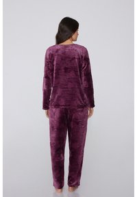 Conjunto de ropa de descanso de terciopelo morado que incluye camiseta de manga larga y pantalones. La tela parece suave y con una superficie texturizada. Detalles mínimos, cobertura completa.