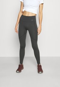 Leggings moulants taille haute en tissu gris foncé avec des coutures courbées. Associés à des chaussures de sport bourgogne et un t-shirt blanc.