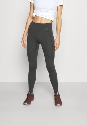 Tight-fitting, high-waisted leggings in dark gray fabric with curved seam detailing. Paired with burgundy athletic shoes and a white shirt.
