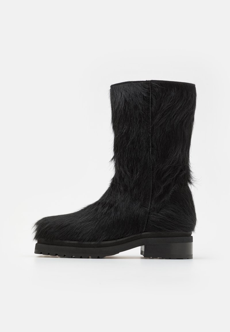 Botte noire en fausse fourrure jusqu'au genou avec une semelle en caoutchouc texturé et plate. Présente un design simple et un bout légèrement arrondi.