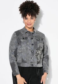 Grå denimjacka med blommig broderi, strukturerade mönster, knäppning framtill och två bröstfickor. Detaljerad design med glänsande accenter.