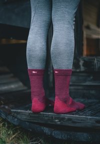 Burgundy crew-socks dengan tekstur ribbed, dengan aksen kontras di jari kaki dan tumit, dipakai dengan legging abu-abu di atas permukaan kayu.