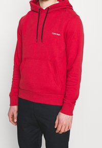 Sudadera de algodón roja con un bolsillo frontal, capucha con cordón, puños elásticos y un pequeño logo blanco de Calvin Klein en el pecho.