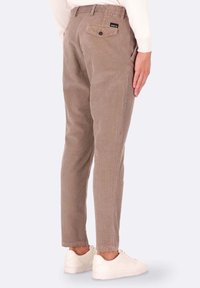 Pantaloni in velluto a coste marroni con strisce verticali strette, dotati di tasca posteriore con bottone e un design aderente. Indossati con sneakers bianche.