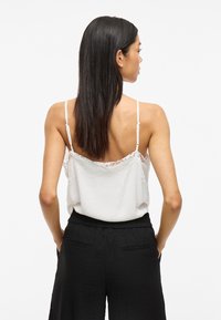 Camiseta blanca sin mangas con encaje y tirantes finos, combinada con pantalones negros de cintura elástica. Tela suave con una silueta relajada.