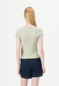 Light green fitted t-shirt with short sleeves and a round neckline, paired with dark blue denim shorts. Simple, smooth fabric texture.