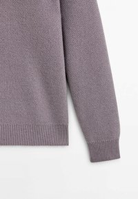 Pull-over en maille violet clair, avec un motif texturé et des poignets côtelés. Le tissu semble doux et léger.