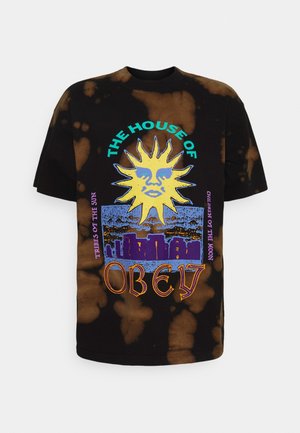 T-shirt tie-dye nera e marrone con grafica di volto di sole giallo, skyline blu e testo con scritto "The House of Obey" e altre frasi.