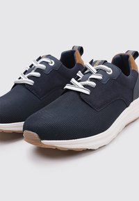 Zapatillas de malla en color marino con cordones blancos, un acento en el talón color beige y una suela blanca acolchada, que presentan una parte superior texturizada para mayor transpirabilidad.