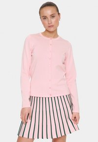 Cardigan côtelé rose clair avec un col rond et une fermeture à boutons sur le devant, associé à une jupe plissée à rayures verticales vertes.