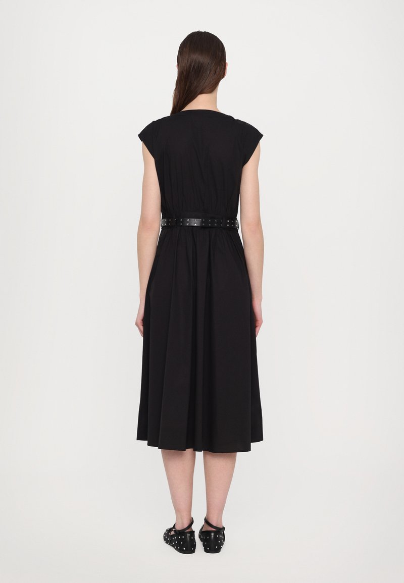 Vestido negro con mangas cortas tipo capa, cintura fruncida y falda fluida; cuenta con un cinturón negro brillante con acentos de tachuelas; se lleva con zapatos casuales.