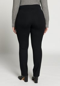 Schwarze enge Hosen mit hohem Bund, glatter Textur und elastischem Stoff. Getragen mit einem grauen Langarm-Oberteil und schwarzen Absatzschuhen.
