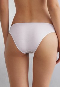 Bílé bavlněné spodní prádlo ve stylu bikiny se hladkým povrchem, nízkým pasem a minimalizovanými švy, umístěné na neutrálním pozadí.