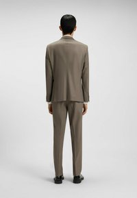 Slim-fit, gray-brown suit with a smooth texture, jacket featuring single vent, and matching trousers. Black shoes complete the look.
