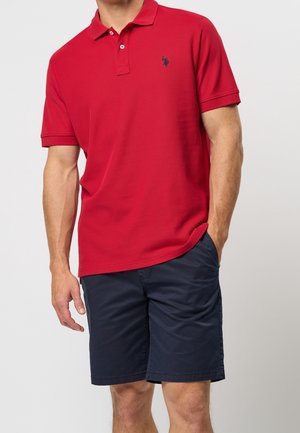Polo rouge avec deux boutons, tissu texturé et logo bleu marine. Associé à un short bleu marine, avec une coupe décontractée et des poches.