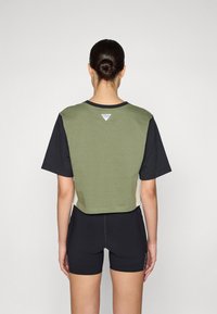 T-shirt cropped con parte superiore verde e maniche nere, con un piccolo logo bianco sul retro, abbinato a pantaloni corti neri.