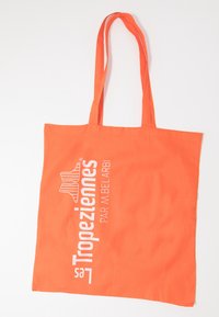 Bolso tote naranja brillante con asas largas, con el texto blanco "Les Tropeziennes PAR M. BELARBI" y un logo de sandalia a rayas en el frente.