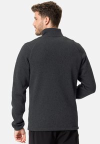 Veste en polaire gris foncé avec un col haut, des manches longues, un tissu texturé et un ourlet légèrement allongé à l'arrière. Design simple.