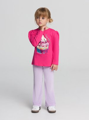 Camicia rosa a maniche lunghe con grafica di cupcake e testo, abbinata a pantaloni di velluto a coste viola chiaro e sneakers bianche. Tessuto liscio e vestibilità casual.