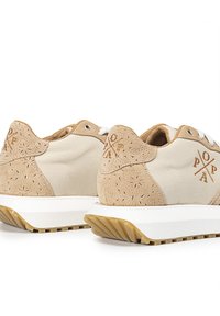 Zapatillas beige con una combinación de lona suave y ante texturizado, con perforaciones decorativas, cordones blancos y una suela blanca.