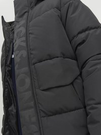 Black puffer jacket with a quilted texture, featuring a prominent logo print and a zippered front. Includes a patch pocket on the chest.