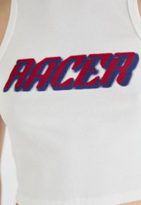 Hvit ribbestrikket crop topp med "RACER" i fet rød og blå skrift, som fremhever tekstur og livlig fargekontrast.