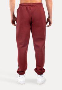 Vinröda joggerbyxor med resår i midjan, muddade anklar och en slät textur, kombinerade med vita sportskor.