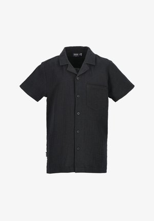 Schwarzes kurzärmeliges Hemd mit Knopfleiste und Tasche, blaue Jeans und weiße Turnschuhe mit schwarzen Streifen und hellbraunen Sohlen. Schlichter weißer Hintergrund.