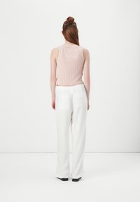 Light pink ribbed tank top paired with loose white trousers featuring side pockets. The top has a curved hem and slender straps.