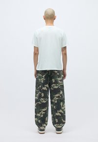 Gai pelēks īsība t-krekls un brīvi pieguļoši kamuflāžas šorti ar vairākiem kabatām, uz vienkārša balta fona.