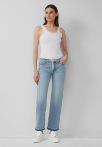 Witte tanktop met kantafwerking, lichtblauwe rechte jeans met wijde pijpen en witte sneakers. Eenvoudig ontwerp met een losse pasvorm en rechte snit.