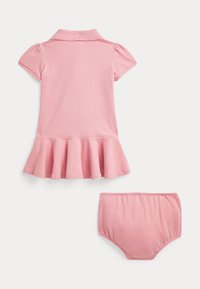 Vaaleanpunainen puuvillainen polomekko, jossa on lyhyet liehukkeet hihat ja levenevä helma, mukana sopivat tamponishortsit. Sileä tekstuuri, yksinkertainen muotoilu.