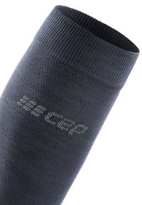 Kompressionssocke aus dunkelgrauem Stoff, gerippte Textur, mit einem Logo in hellgrau an der Seite. Abgerundete Öffnung am Bund oben.