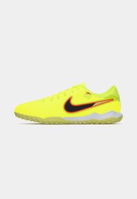 Botín de fútbol de césped en color amarillo neón de Nike, con el logo de swoosh en negro y rojo, diseño de cordones y suela texturizada para mayor tracción en superficies artificiales.