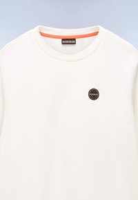 Sudadera color crema con cuello redondo, que presenta un pequeño parche de logo en negro y marrón. Tejido suave y texturizado con un acento naranja en el interior del cuello.