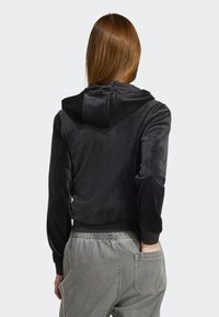 Black velvet cropped hoodie with a soft texture, featuring a hood and ribbed hem. Worn with light gray elastic waist pants, showing a back view.