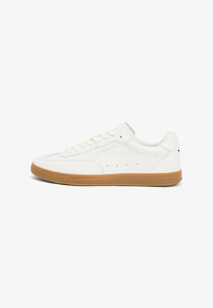 White low-top sneaker with gum sole, lace-up closure, and "Tommy Hilfiger" branding on the side.