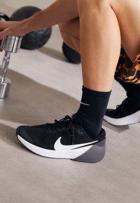 Černá běžecká obuv Nike s bílým swooshem, texturovaným svrškem a polstrovanou podrážkou. Doplněno černou ribovanou ponožkou.