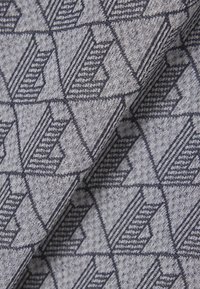 Prim-plan al unui material gri cu un model geometric de triunghiuri suprapuse alb-negru și detalii tricotate texturate.