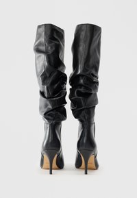 Black leather knee-high boots with a slouchy design, pointed toe, and thin stiletto heel. Features smooth texture and minimal hardware.