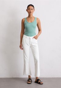 Débardeur bleu clair, jeans blancs coupés avec des ourlets effilochés, sandales noires avec une boucle dorée. Tissu lisse et design ajusté.