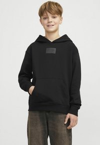 Sudadera negra con capucha y bolsillo tipo canguro, que presenta un parche de logo cuadrado en el pecho. Puños y dobladillo acanalados con un ajuste relajado.