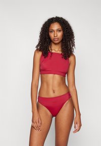 Ensemble de bikini rouge comprenant un haut à encolure carrée et un bas taille haute, fabriqué en tissu lisse et extensible avec des coutures minimales.